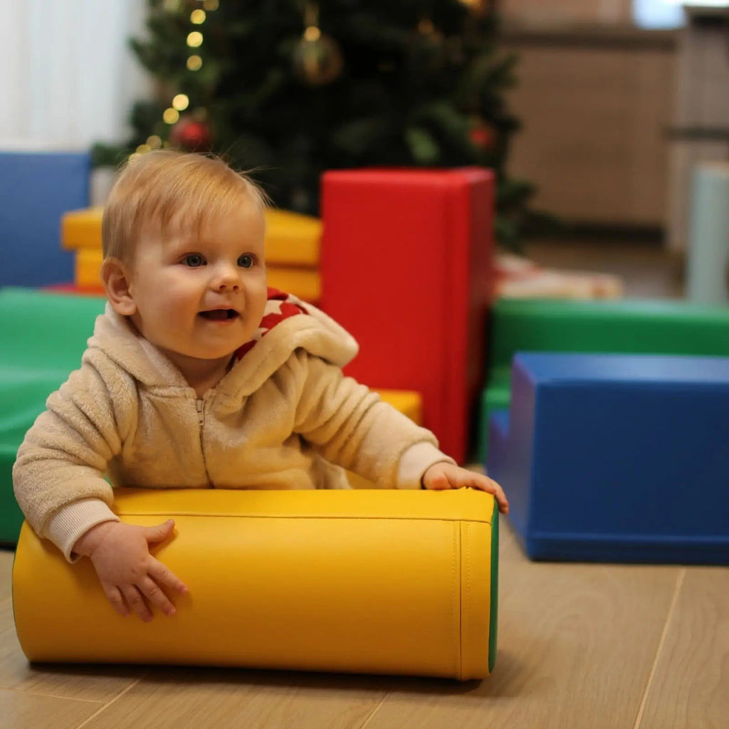 1. Baby playing with yellow foam cylinder near Christmas tree