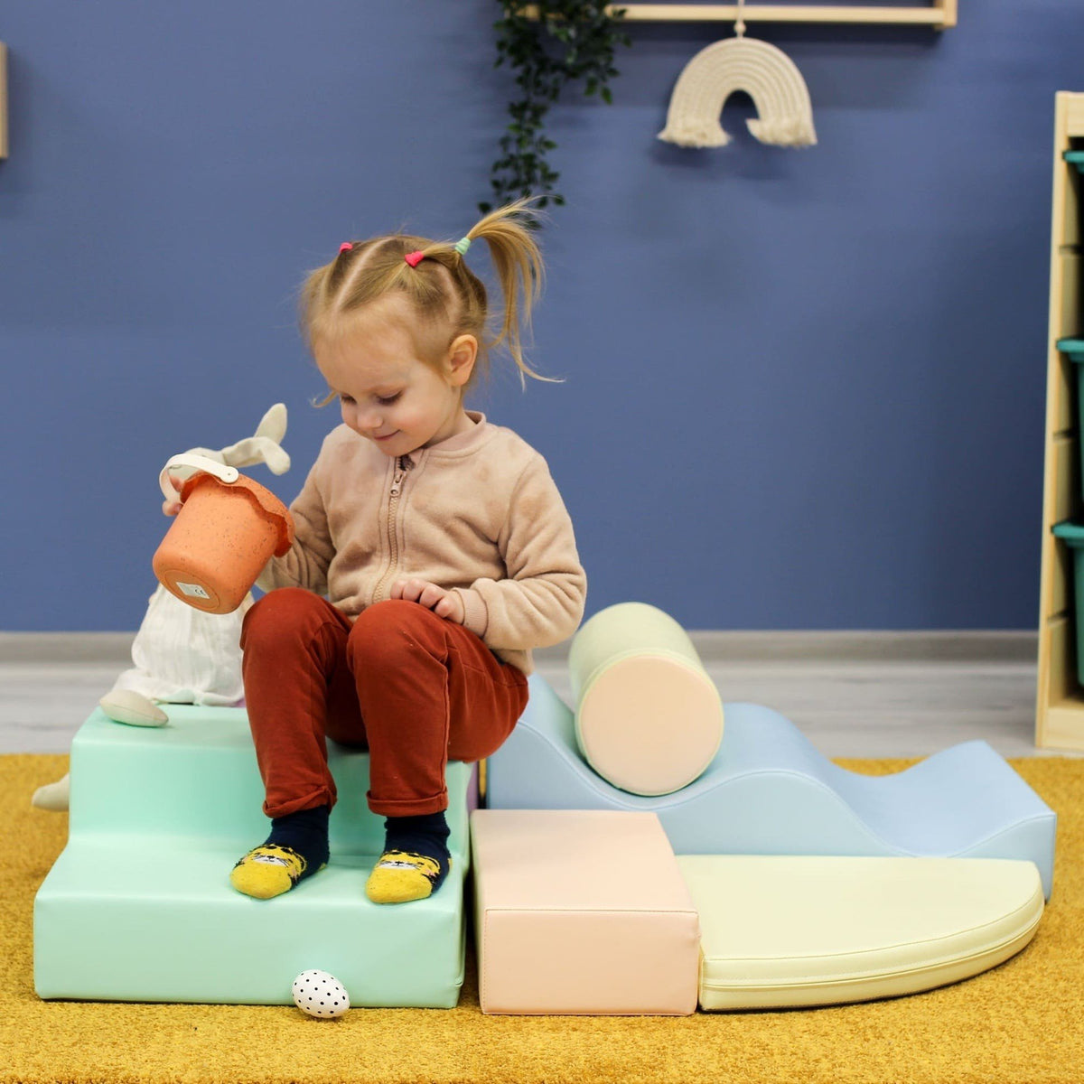 1. Child sitting on pastel foam blocks in a colorful playroom