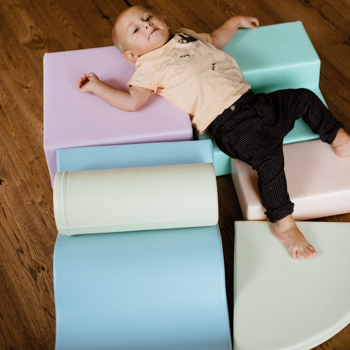 1. Child lying on pastel foam blocks on a wooden floor