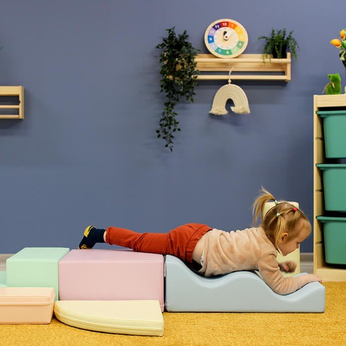 1. Child lying on pastel foam blocks in a colorful playroom