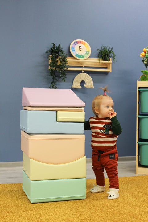 1. Child standing next to stacked IGLU Little Crawler pastel foam blocks in a playroom