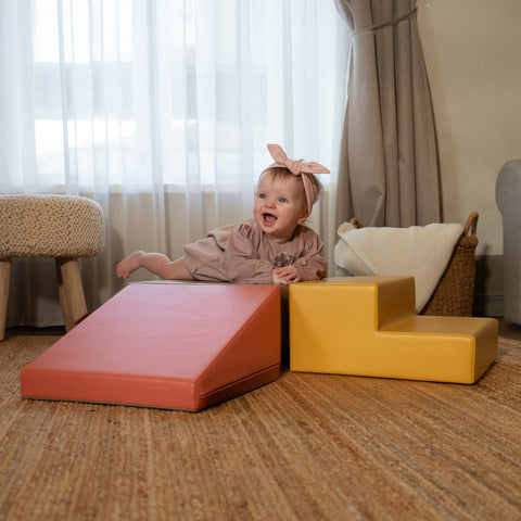 1. Baby girl in pink outfit smiling while playing on IGLU pastel pink and yellow foam blocks in a cozy room