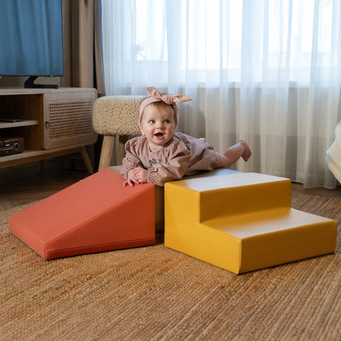 1. Baby girl in pink dress with headband lying on IGLU pastel pink and yellow foam blocks in a living room