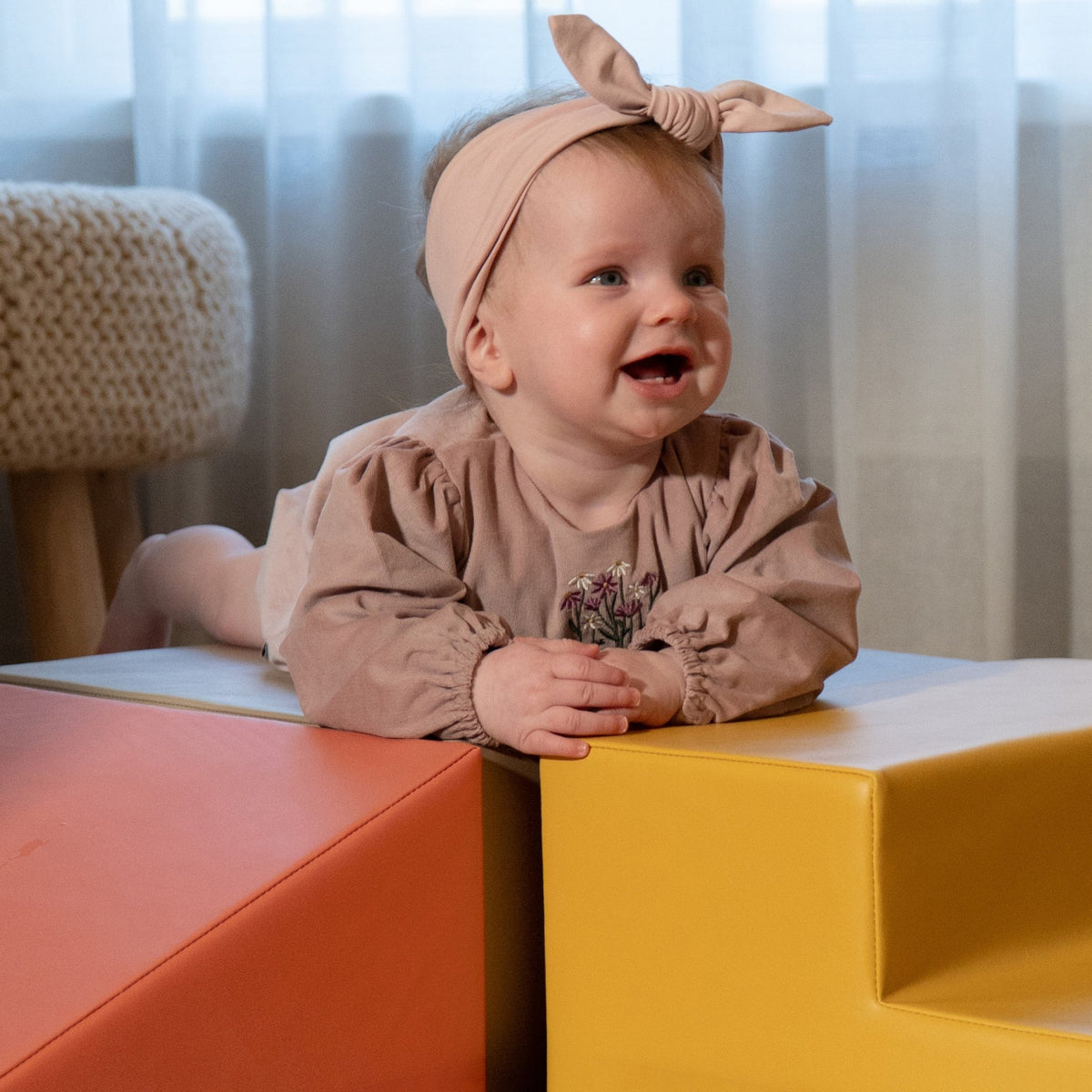 1. Close-up of baby girl in pink dress smiling on IGLU pastel pink and yellow foam blocks