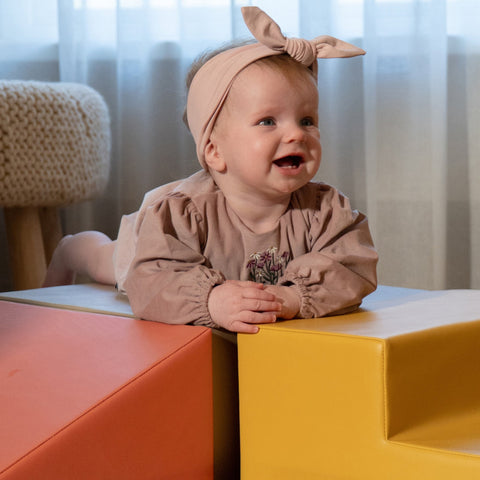 1. Close-up of baby girl in pink dress smiling on IGLU pastel pink and yellow foam blocks