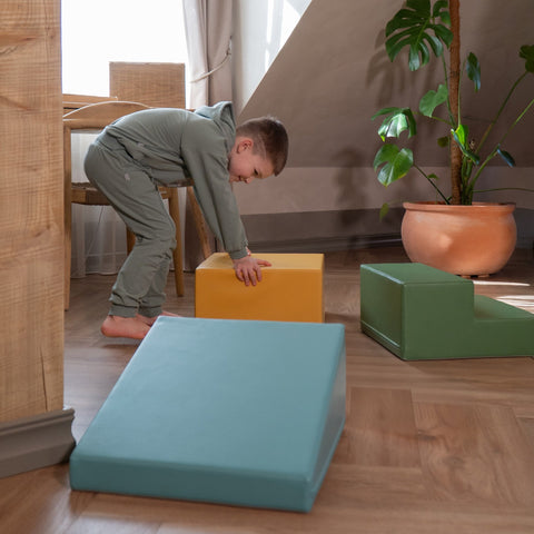 3. Child in grey outfit playing with IGLU pastel turquoise, yellow, and green foam blocks in a living room