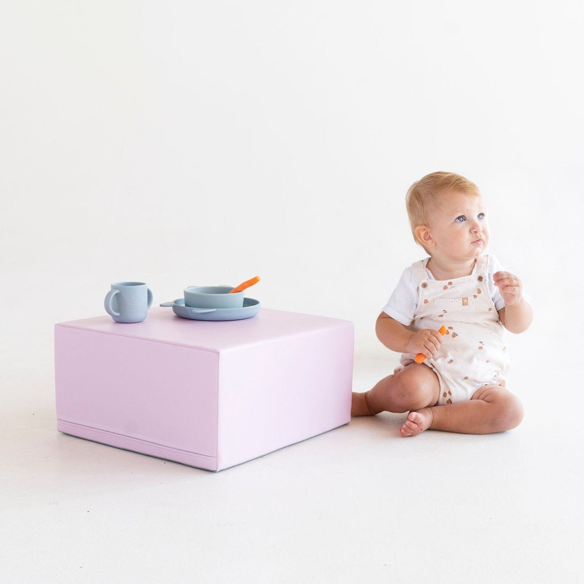 1. Baby sitting beside a pink IGLU foam block with a cup and bowl on top in a studio setting
