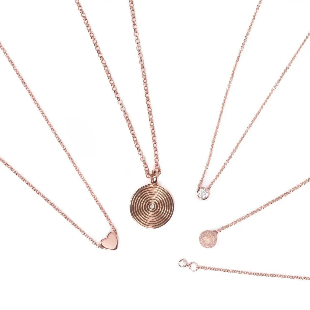 5. Flat lay of MyaMoon Illumi Infinity Pendant Necklace in rose gold with other jewelry pieces