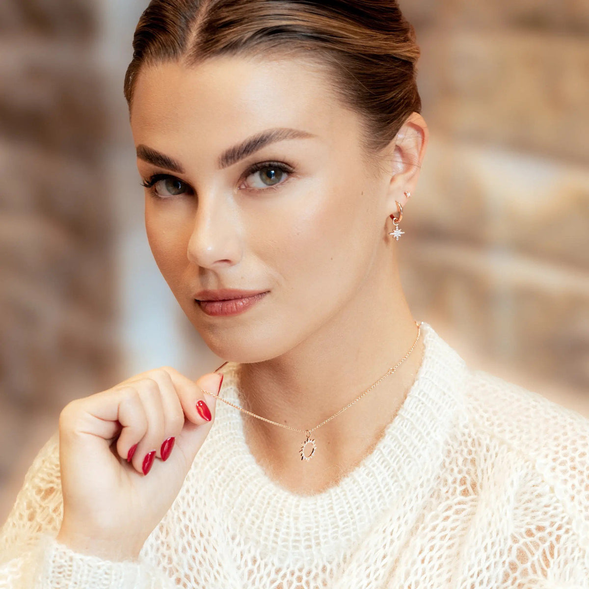 1. Woman wearing rose gold star charm hoop earrings and holding necklace in cozy indoor setting