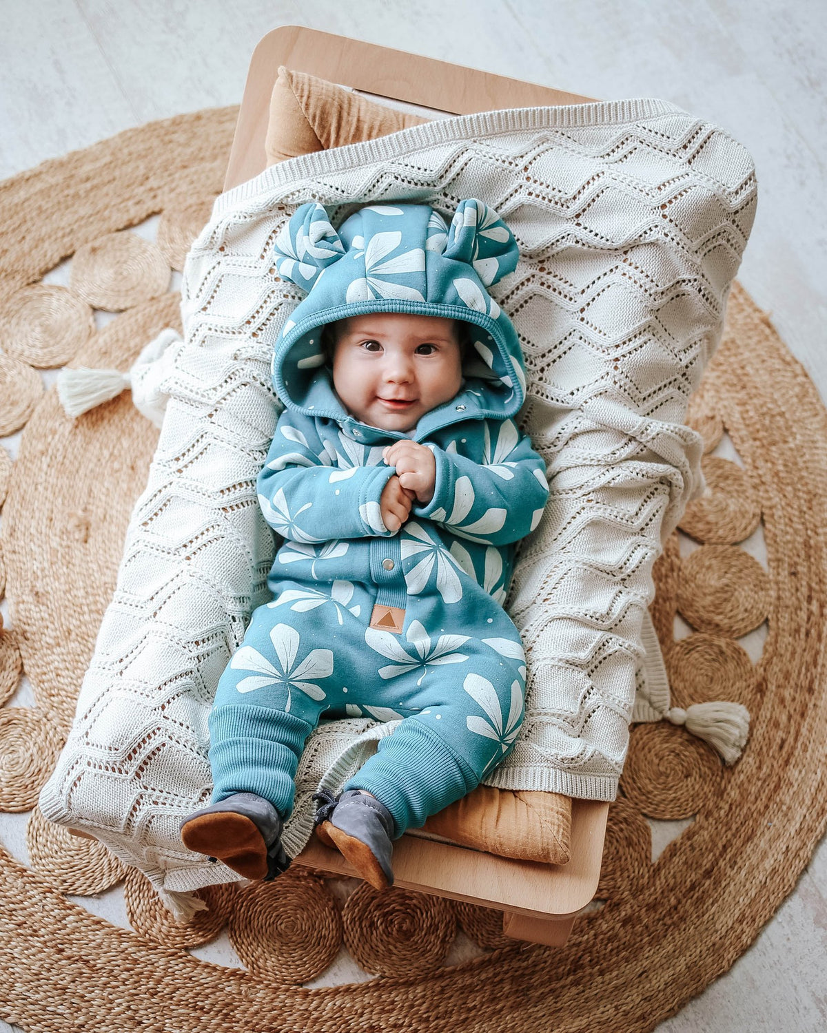 2. Baby lying on knitted blanket wearing green jumpsuit with chestnut leaf pattern and hood with ears