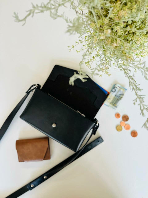 2. Flat lay of KOKUKA crossbody leather bag in black with wallet and coins, showcasing interior compartments