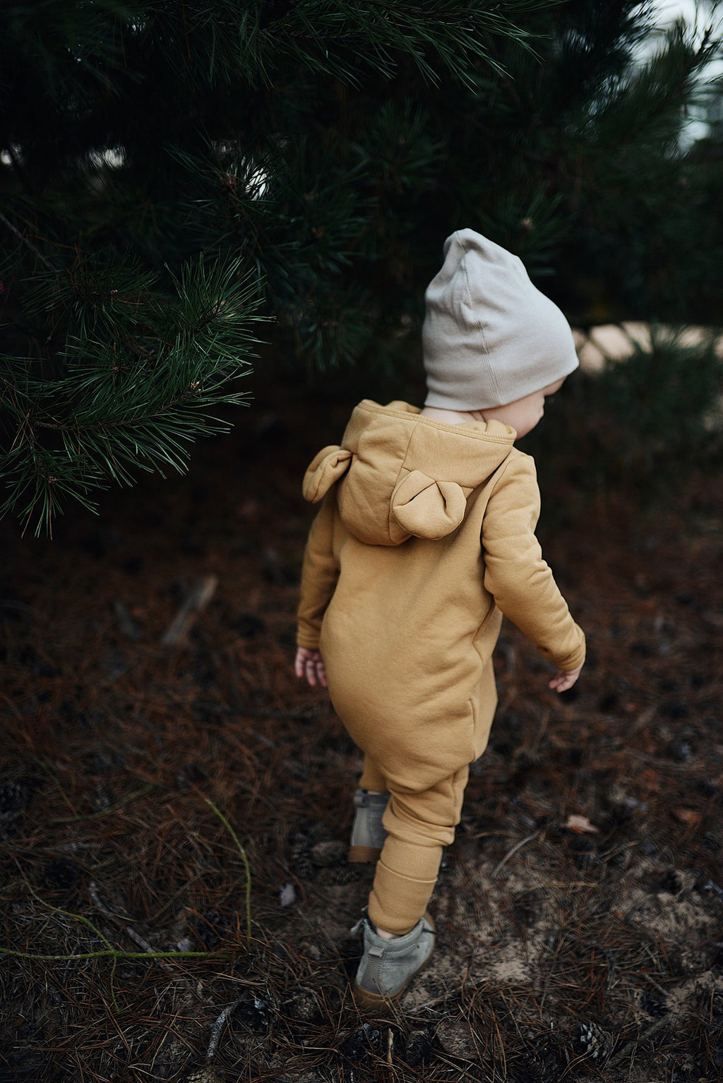 2. Child in mustard eared jumpsuit walking outdoors under pine tree