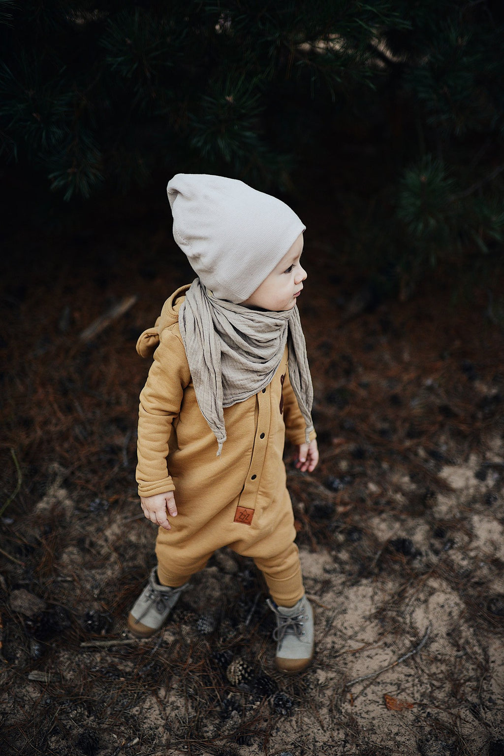 4. Child in mustard eared jumpsuit with hat and scarf in forest setting
