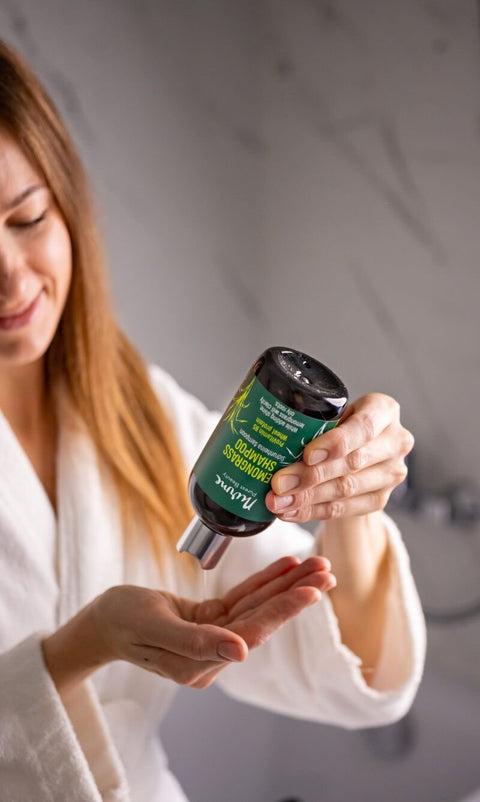 3. Woman in a white robe pouring Nurme Lemongrass Shampoo into her hand, showcasing product use