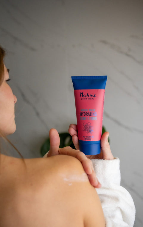 4. Woman holding Nurme hydrating body lotion with Monoi oil, applying to shoulder in lifestyle setting