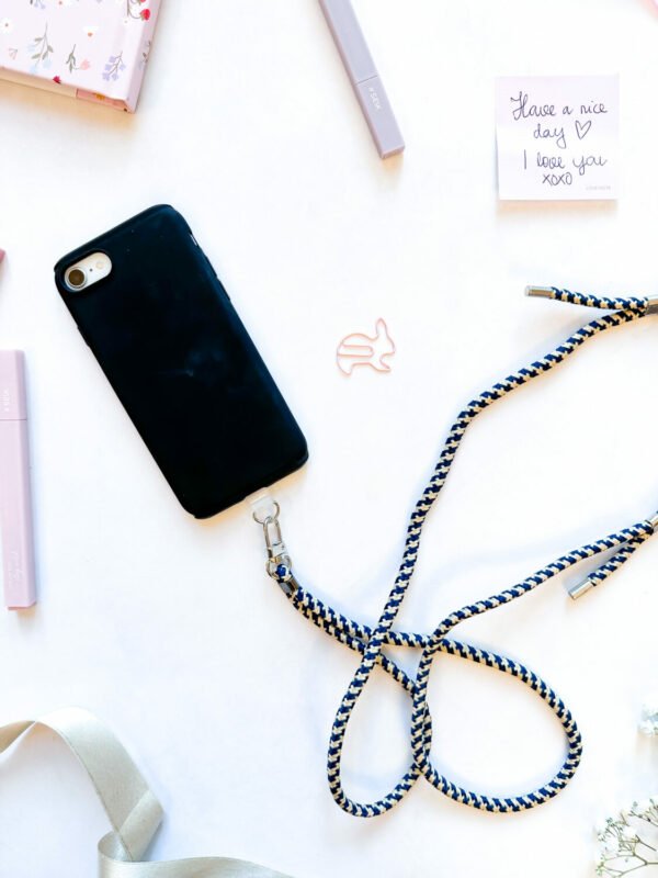 3. Flat lay of SEIK Universal Phone Strap in Sea Edge with black phone case and accessories
