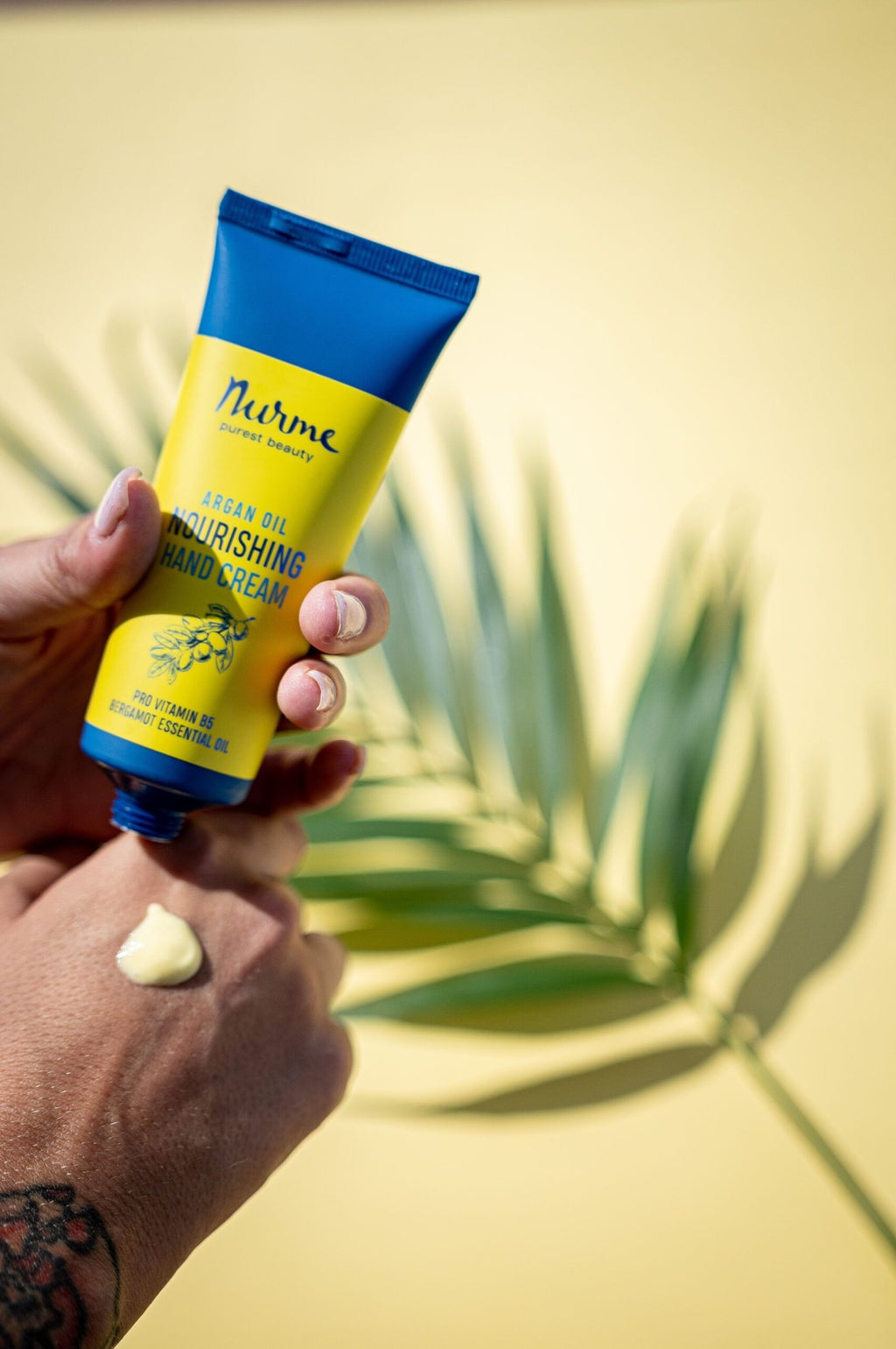 1. Nurme argan oil nourishing hand cream being applied, with a tropical leaf background