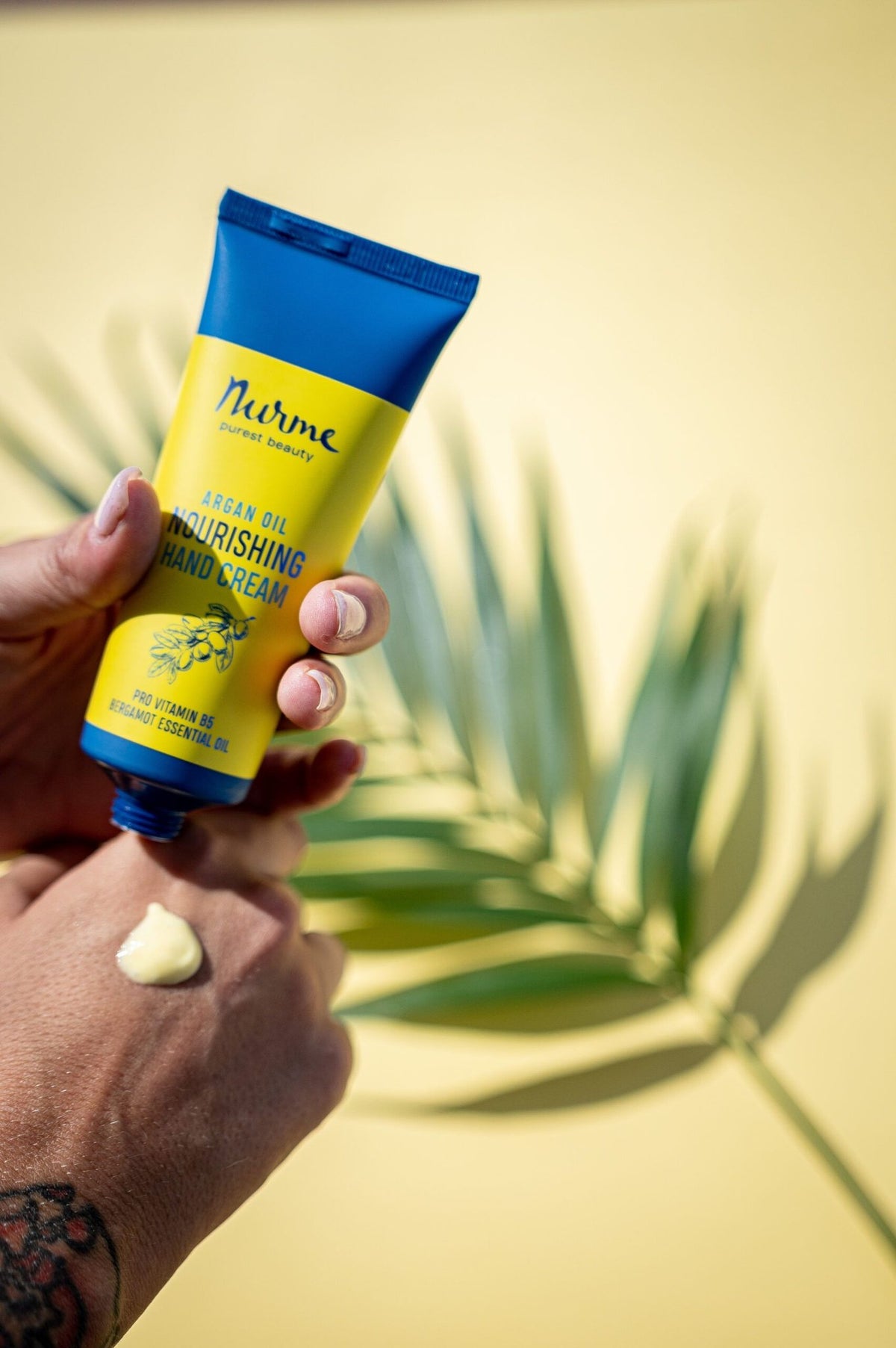 1. Nurme argan oil nourishing hand cream being applied, with a tropical leaf background