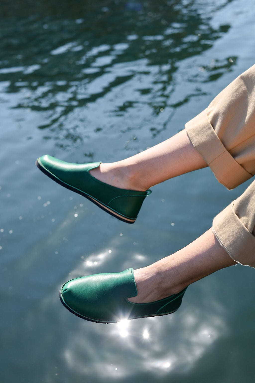 2. Unisex green TOKU London shoes worn by a model with feet dangling over water