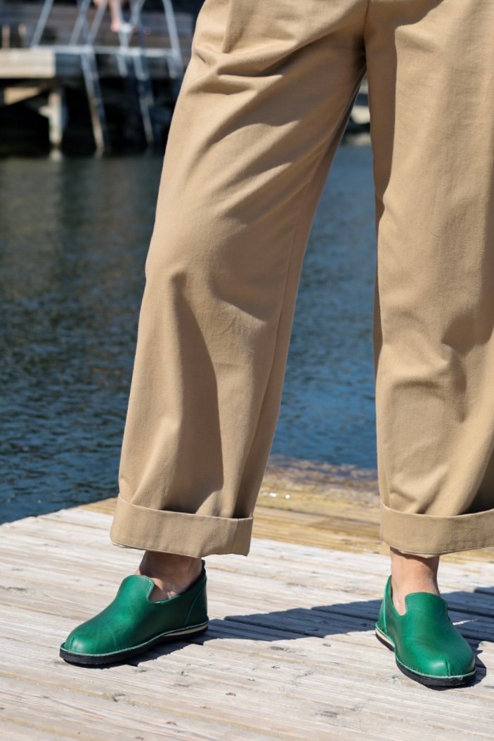 1. Unisex green TOKU London shoes worn by a model on a wooden dock by the water