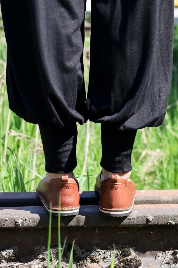 1. Lifestyle image of Omaking London classic brown shoes in TOKU style worn by a person standing on a railway track, shown from the back