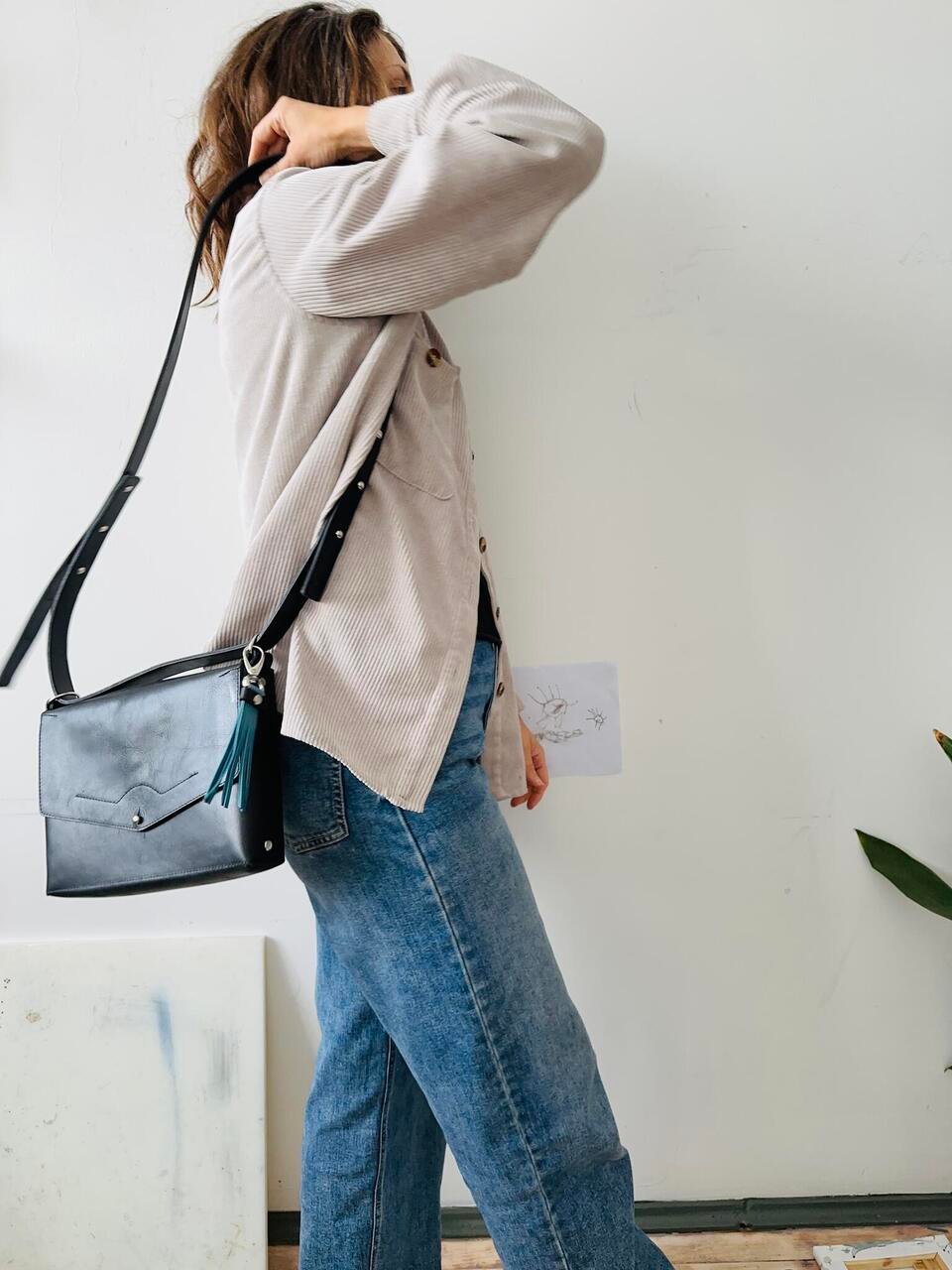 1. Woman wearing eleriinseim KOKUKA crossbody leather bag in black, styled with casual outfit