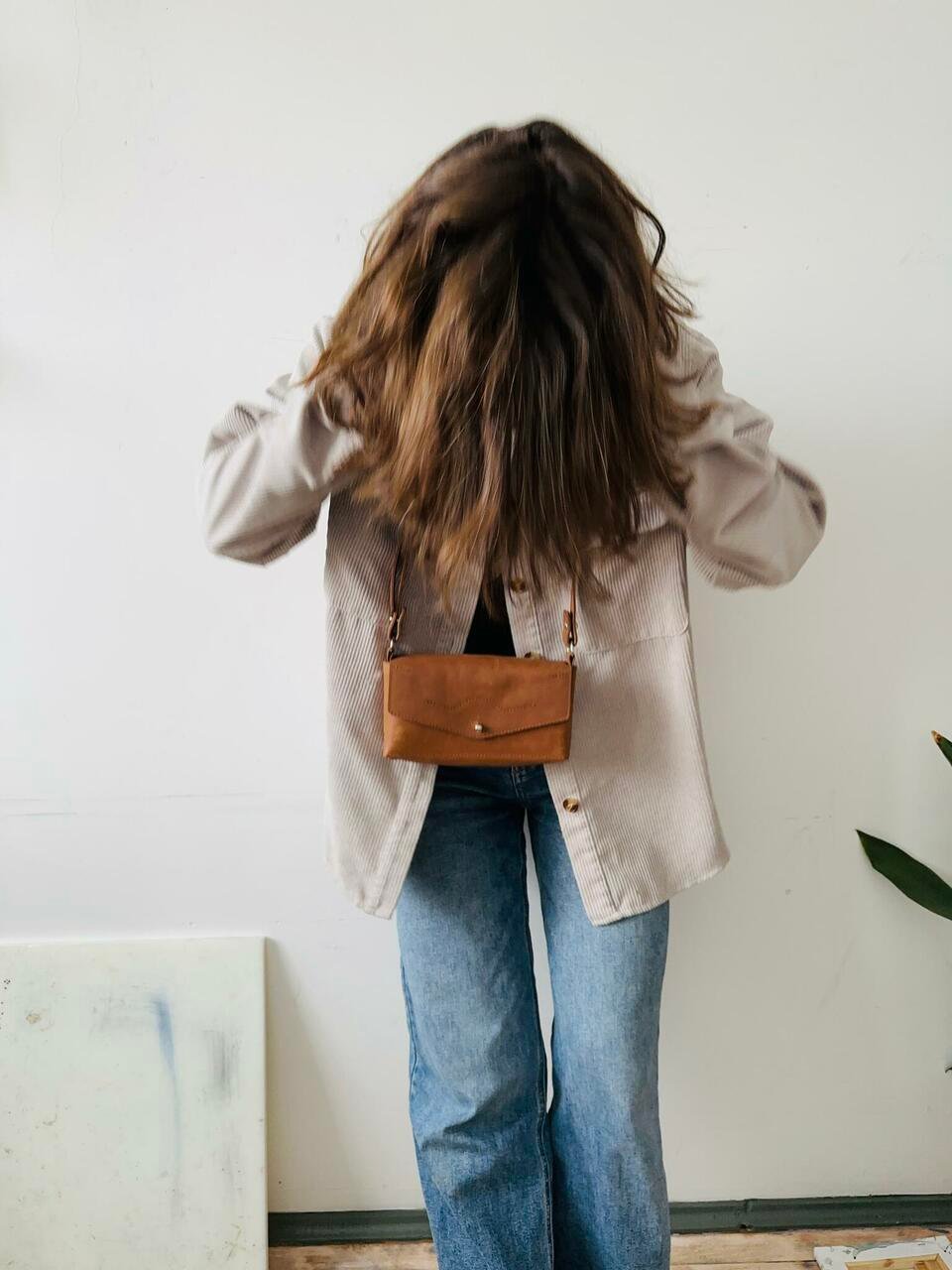 6. Woman wearing KOKUKA crossbody leather bag in tan, styled with casual outfit indoors