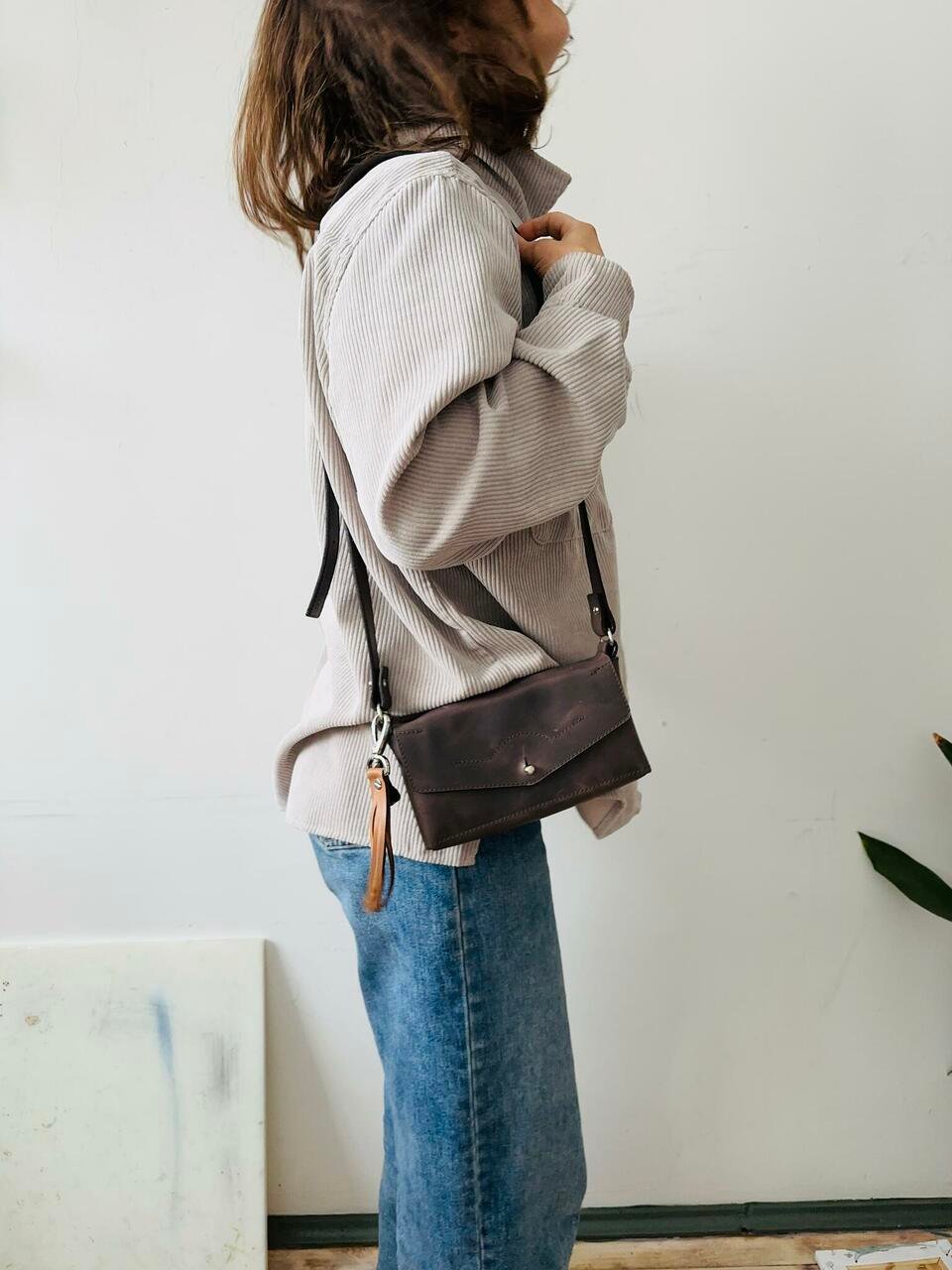 4. Woman wearing KOKUKA crossbody leather bag in brown, shown from the side in a casual setting