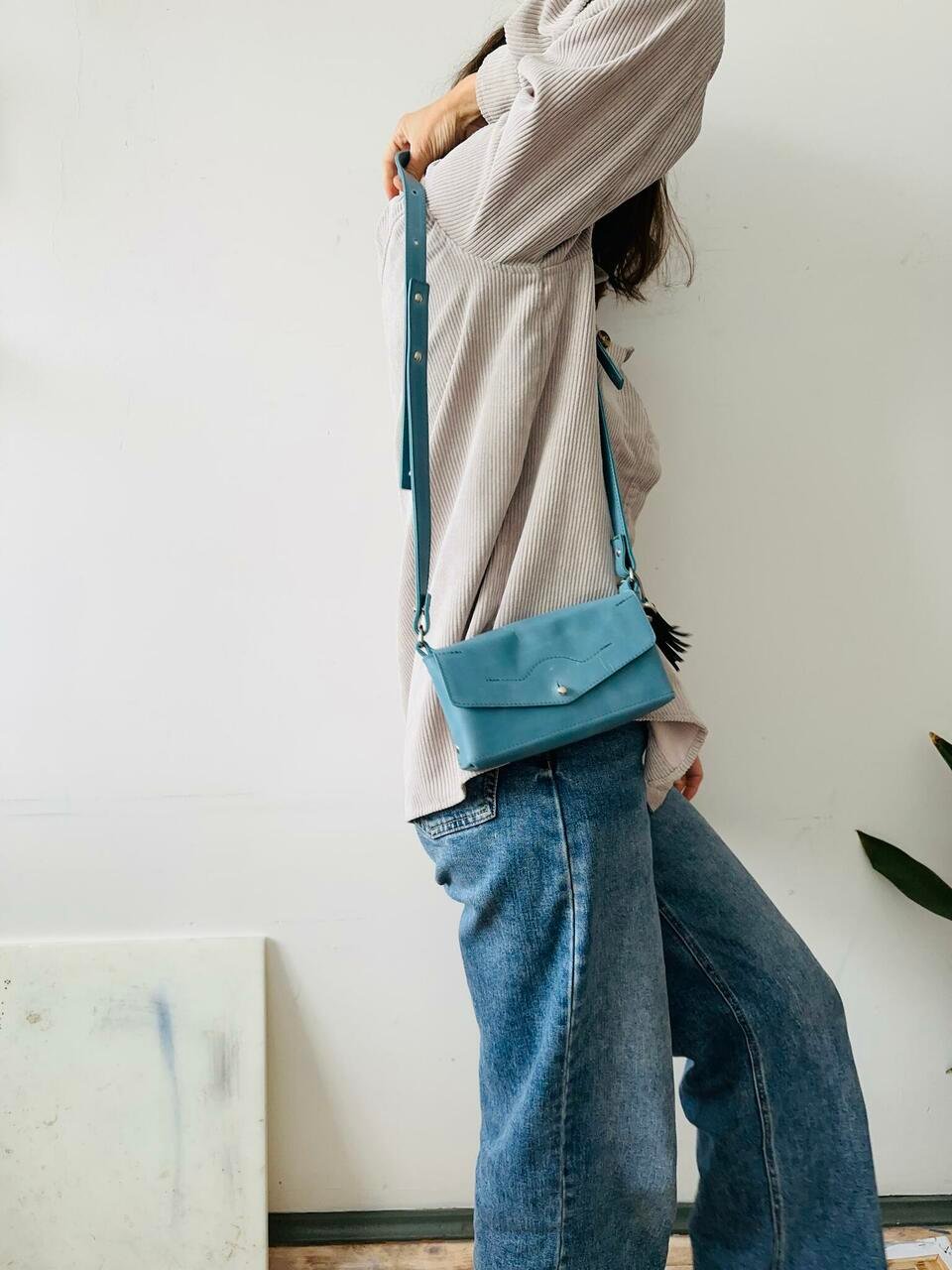 5. Woman wearing KOKUKA crossbody leather bag in blue, styled with casual outfit indoors