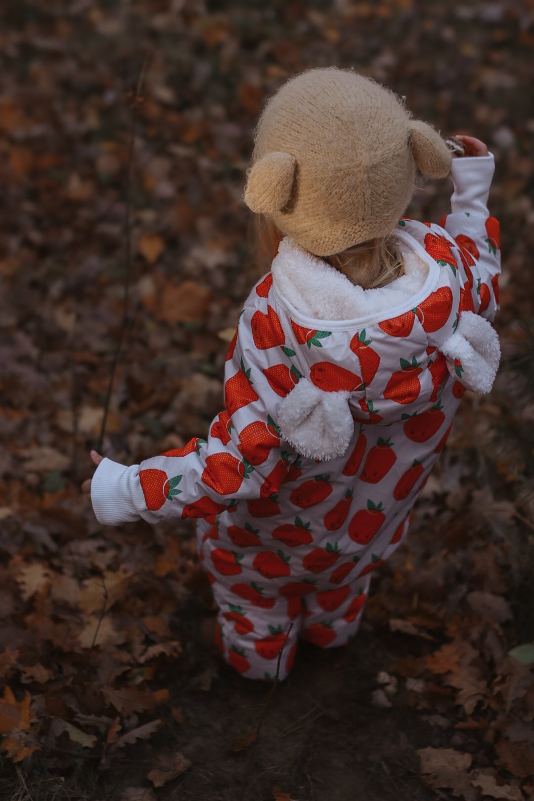 3. Back view of child in Zezuzulla strawberry print jumpsuit with teddy bear ears in a forest