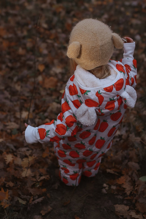 3. Back view of child in Zezuzulla strawberry print jumpsuit with teddy bear ears in a forest