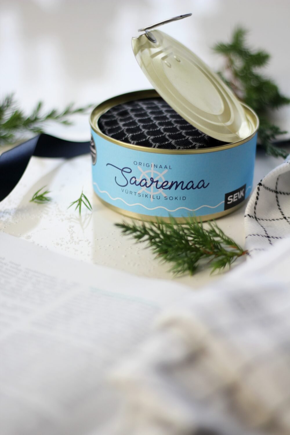 5. Open Saaremaa Vürtsikilu Socks tin showing black patterned socks inside, styled with greenery