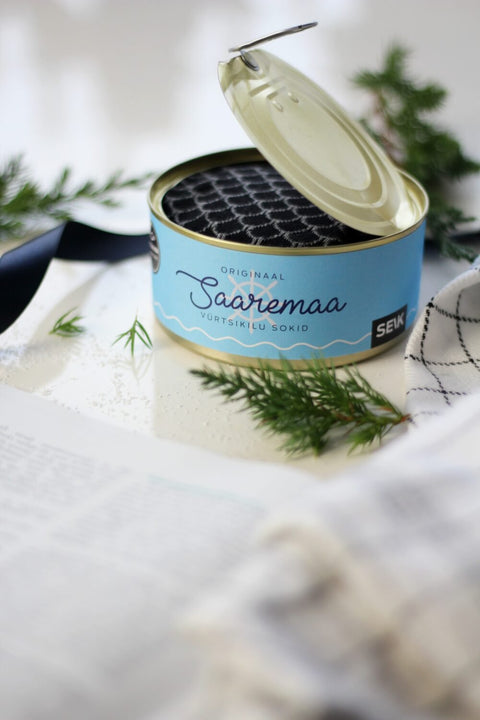 5. Open Saaremaa Vürtsikilu Socks tin showing black patterned socks inside, styled with greenery