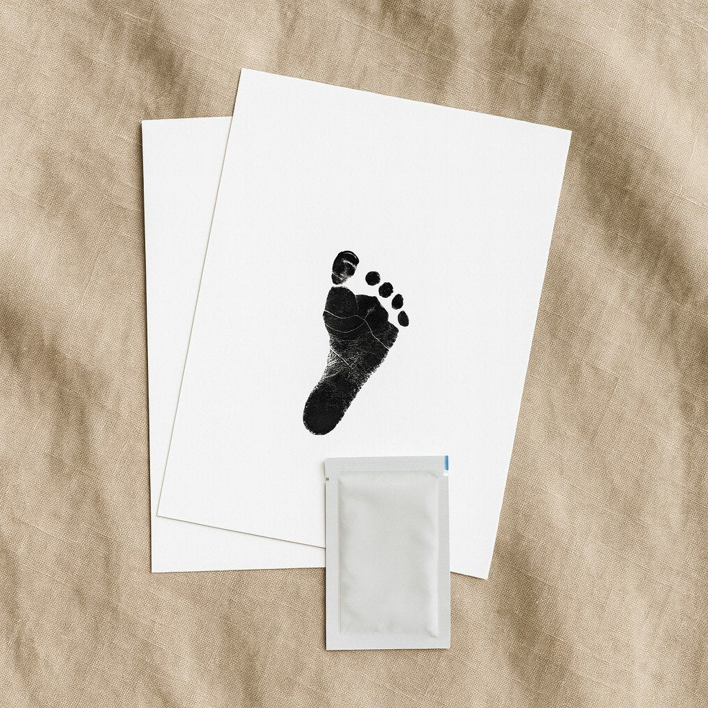 3. Close-up of Beebila ink-free print kit with footprint on white paper and included wipe, on beige fabric