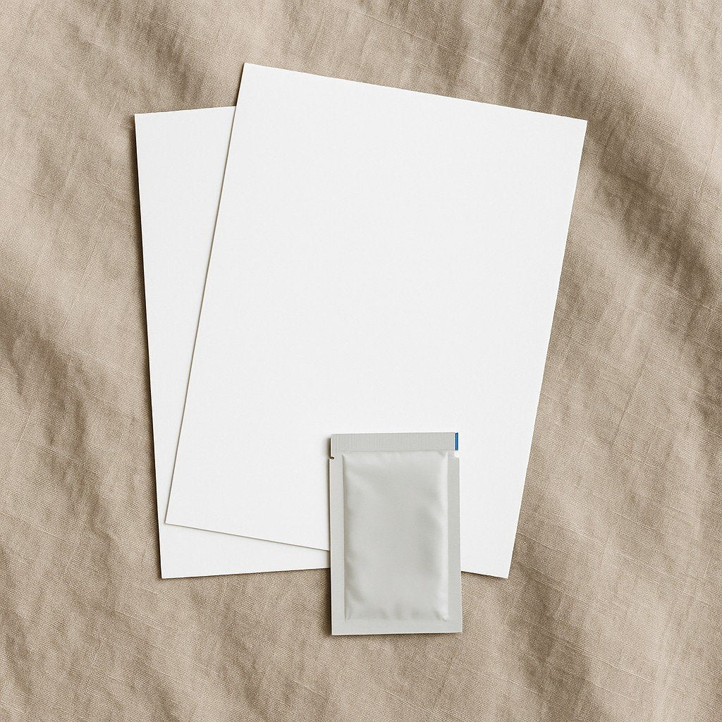 4. Flat lay of Beebila ink-free print kit with two blank imprint papers and wipe on beige fabric