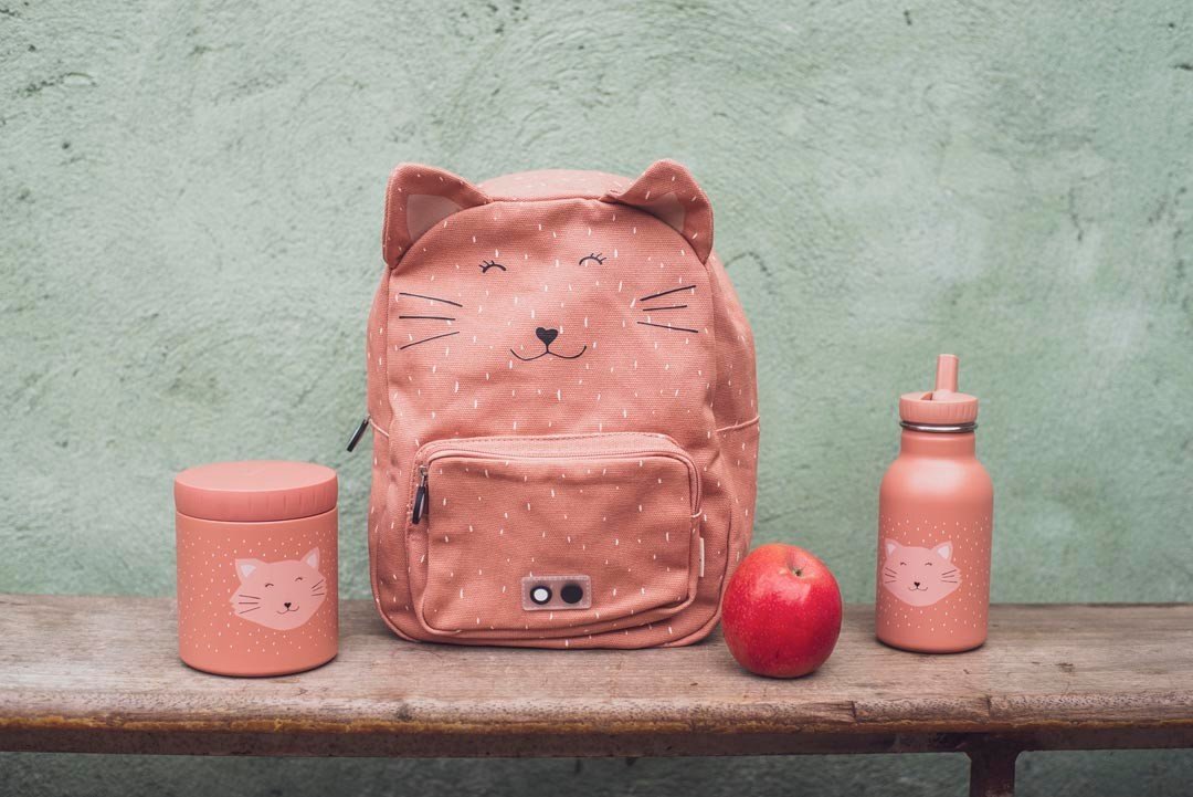 2. Trixie Baby Mrs. Cat lunch pot and bottle next to matching backpack and apple on wooden bench