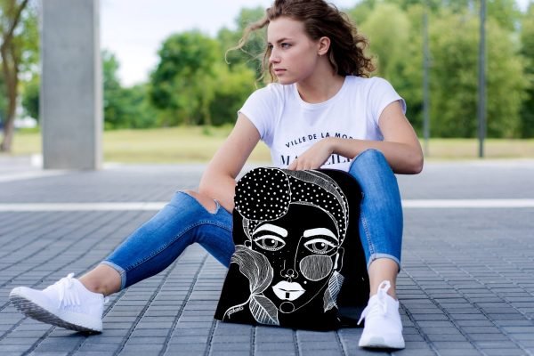 1. Woman sitting outdoors with Garbanota black backpack featuring unique artwork