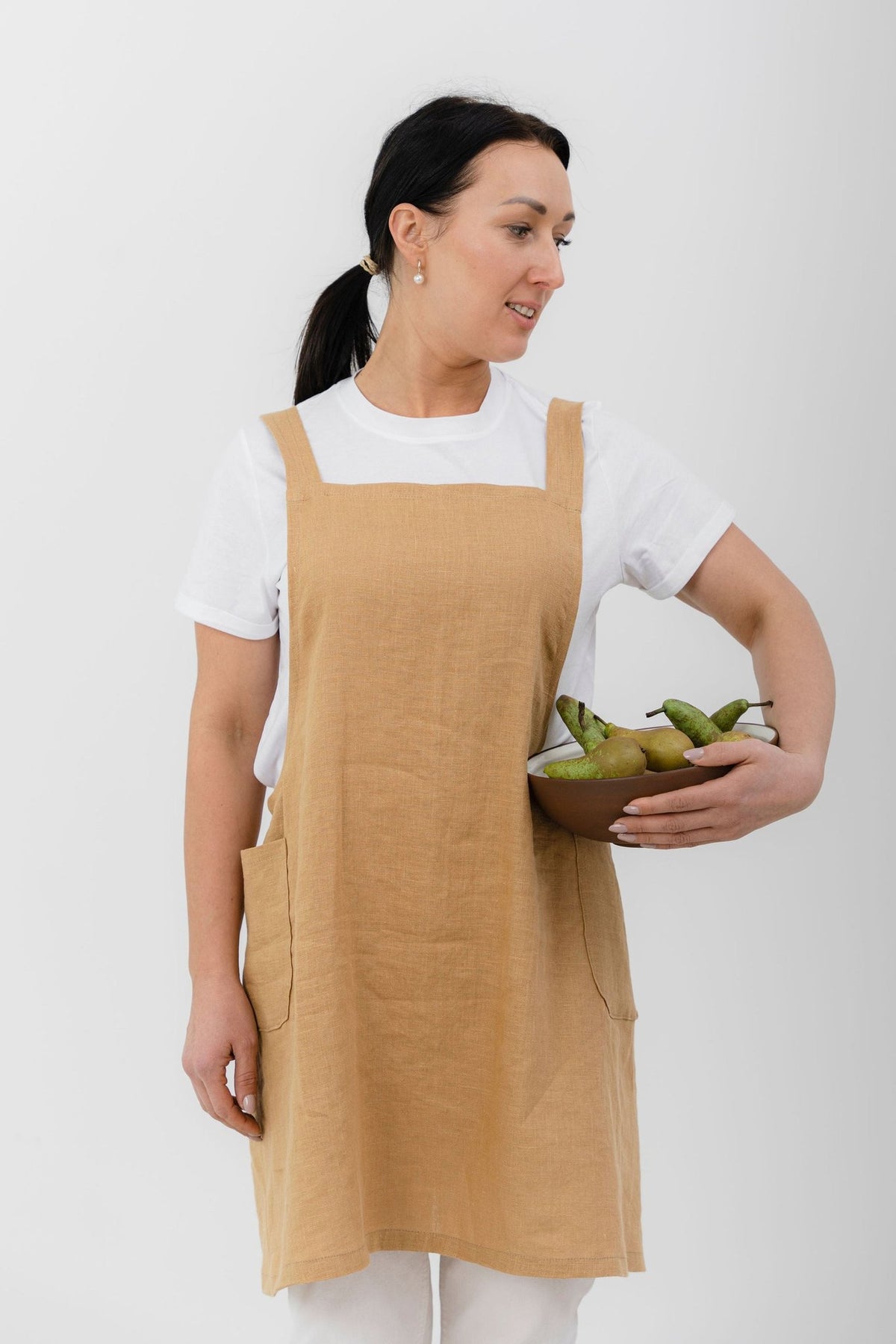 8. Woman in beige Japanese-style linen apron holding pears, standing against white background