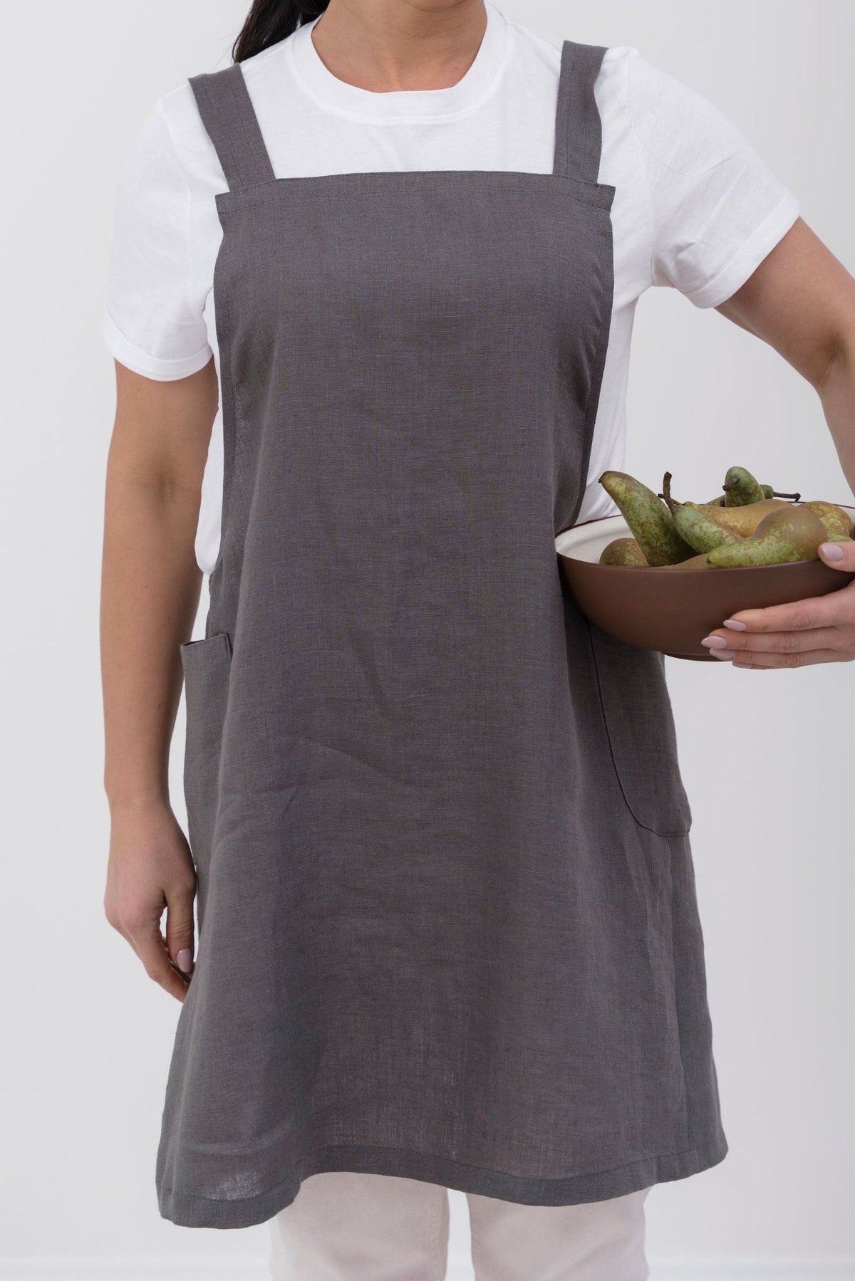 10. Woman in grey Japanese-style linen apron holding bowl of pears, standing against white background