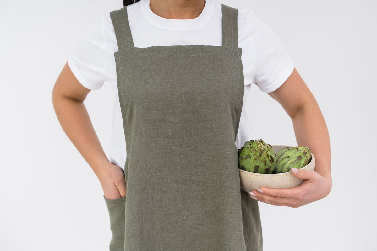 5. Woman in olive green Japanese-style linen apron holding bowl of artichokes, shown from waist up