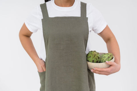 5. Woman in olive green Japanese-style linen apron holding bowl of artichokes, shown from waist up