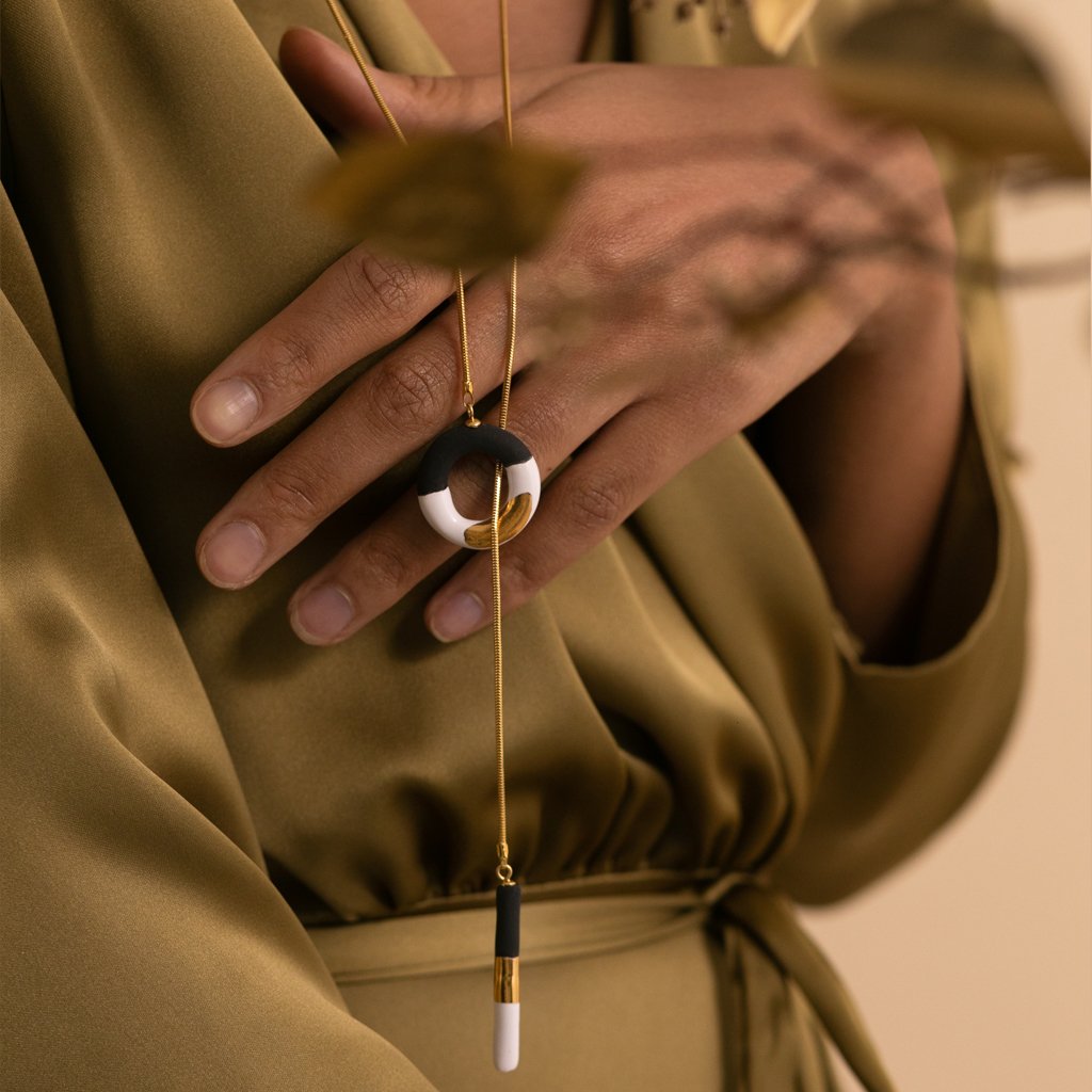 2. Close-up of SCULP Big OM Choker in black and white with 24K gold lustre, held by a woman in a studio setting