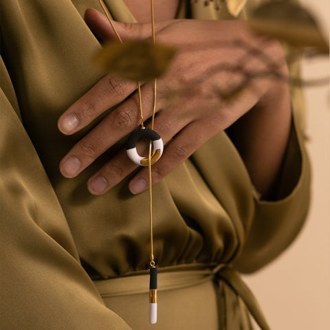 2. Close-up of SCULP Big OM Choker in black and white with 24K gold lustre, held by a woman in a studio setting