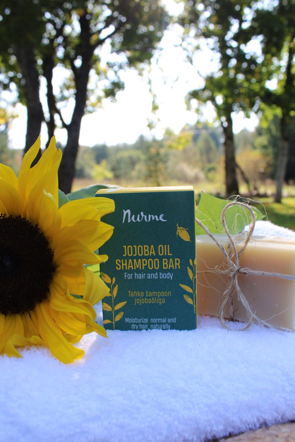 1. Nurme Jojoba Oil Shampoo Bar in green packaging with a sunflower and soap bar on a towel in a sunny outdoor setting