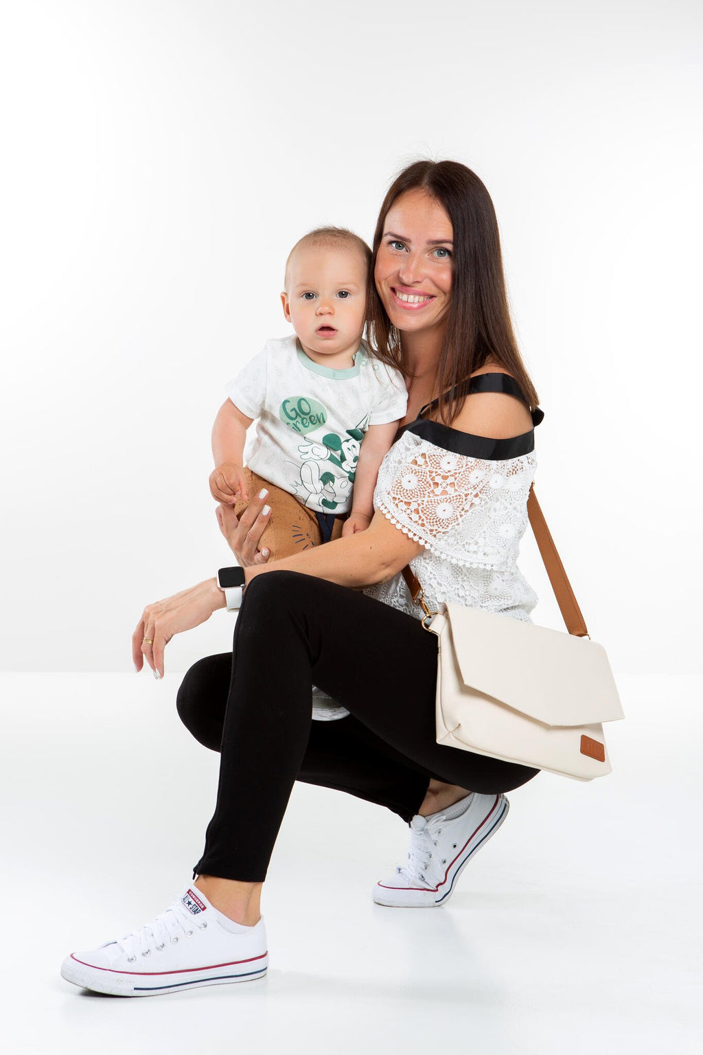 1. Woman holding baby with Ally Scandic Älly Handbag in Cappuccino, showcasing crossbody style in studio setting