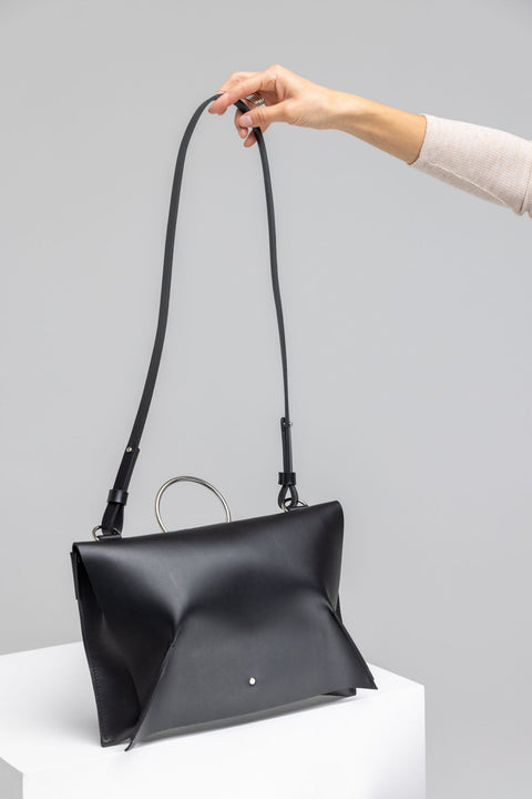 2. Black leather Handbag Kamila by PYKOK with adjustable strap, held by model in studio