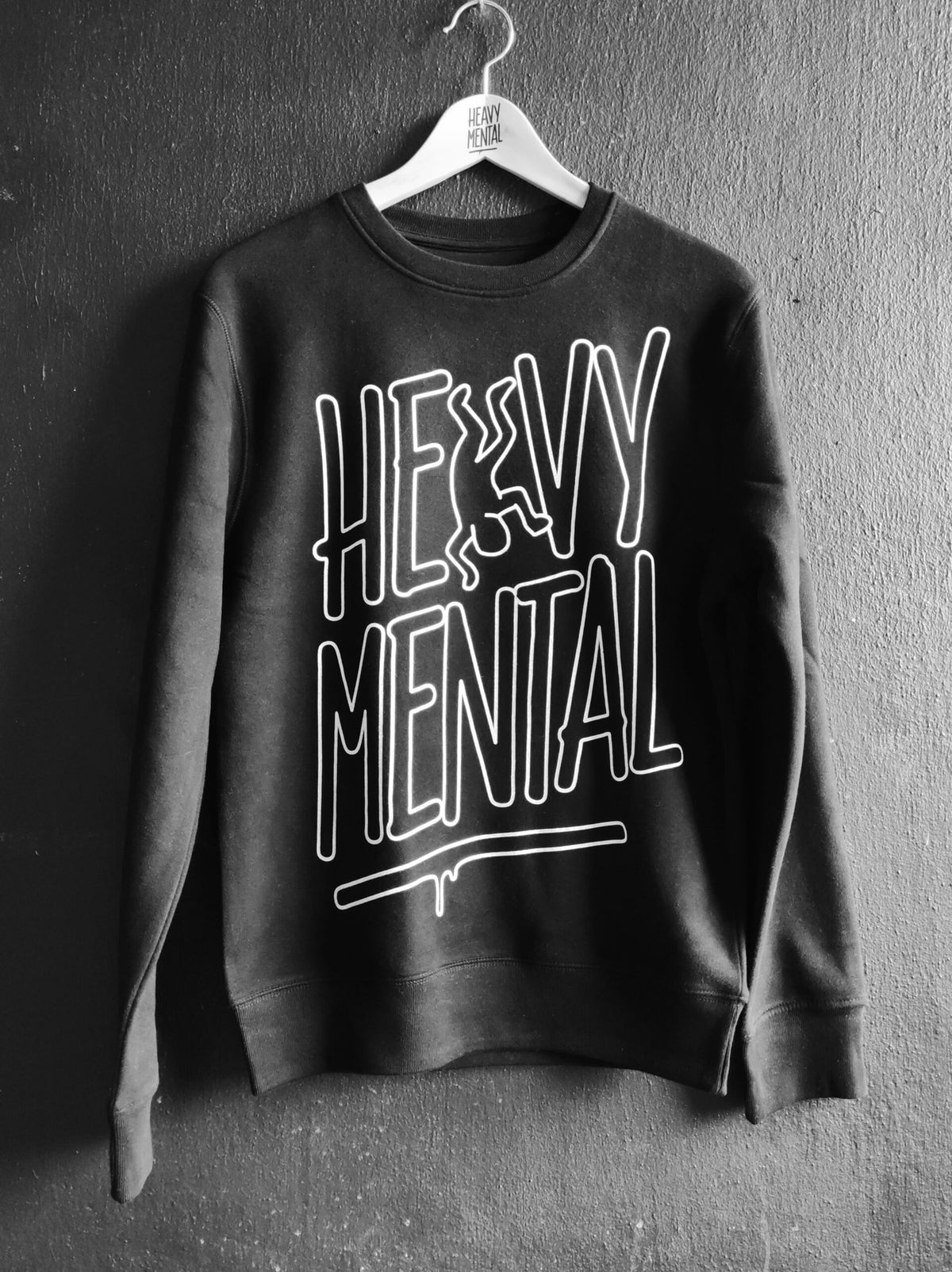 2. Black and white image of Heavy Mental sweatshirt featuring large white lettering, displayed on a hanger