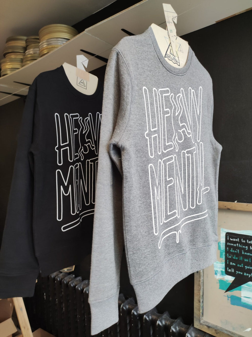 3. Black and grey Heavy Mental sweatshirts with white print, hanging side by side in a studio setting