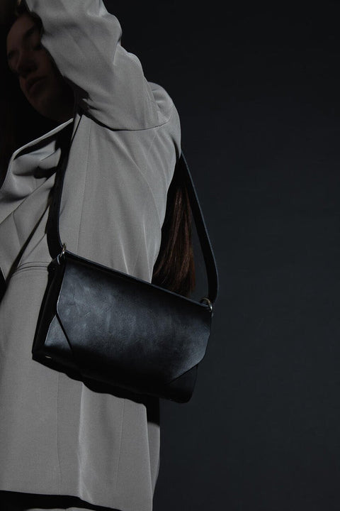 5. Woman wearing black leather Stella Soomlais shoulder bag over light grey blazer in dark studio setting