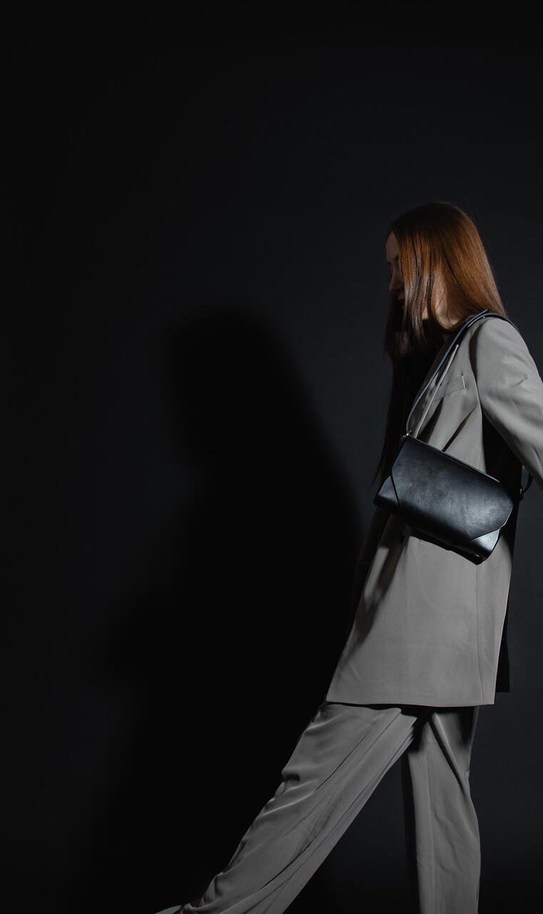 6. Woman in motion wearing black leather Stella Soomlais shoulder bag over grey suit in dark studio
